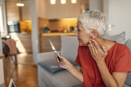 Woman in her 60s looking at her face and neck in the mirror