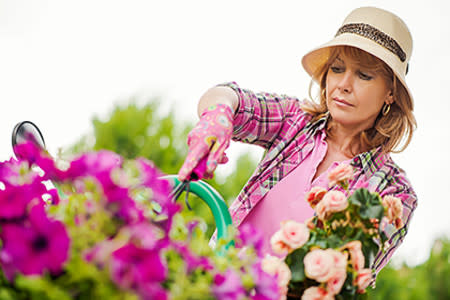 Woman outside working in the garden wearing a hat, gloves, and long-sleeve shirt to protect from the sun