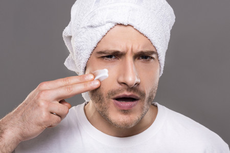 Young man applying lotion on his face