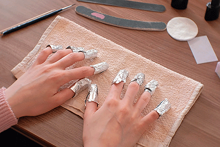 Woman wearing foil nail wraps to remove dip powder nail color