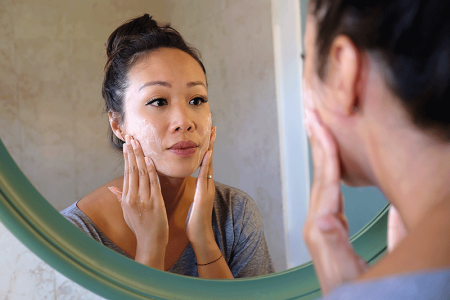 Woman looking in the mirror at rash caused by contact dermatitis.