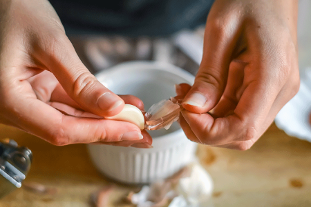 Close-up of woman’s hands peeling garlic, a possible cause of hand dermatitis.