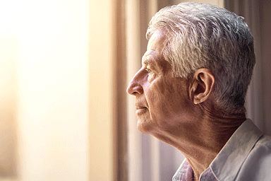 Close up of a senior man looking out of the window at home.