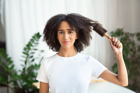 Woman feels dissatisfied by hairstyle, holds hairbrush, combing hair in bathroom.