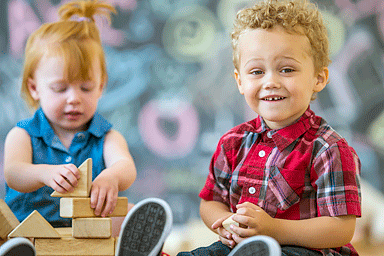 Two toddlers are sharing toys and playing with wood toy blocks at daycare.