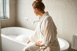 Self-care treatment concept. Side portrait of young woman sitting on tub and touching water before taking bath.