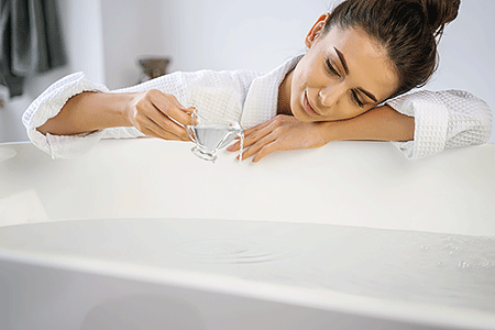 Woman adding bath oil to a bathtub of water