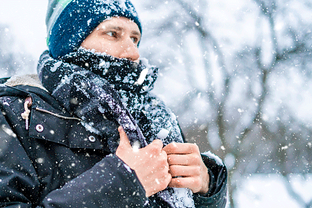 Close up of a man's face with hat and scarf covered by snow on a winter day.