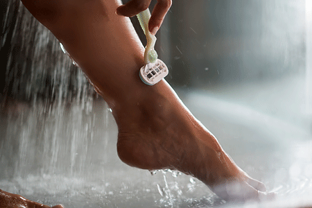 Close up of woman shaving her leg under the shower