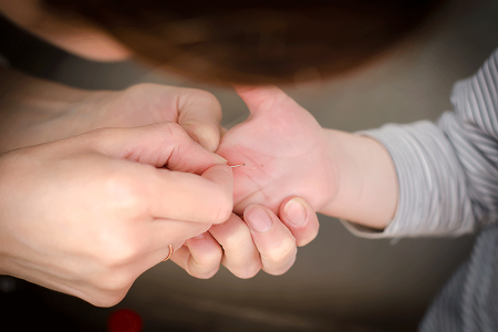 Woman using needle to remove splinter from the hand of a child