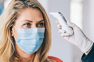 Woman patient wearing medical face mask goes through a temperature check before going into to doctor's office