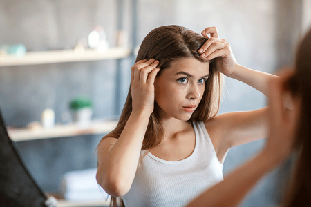 Girl with scalp issues looking in mirror at home.