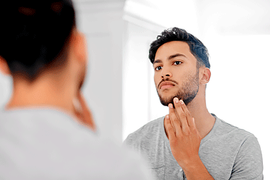 Hombre joven hermoso que mira su cara en el espejo en casa. (Handsome young man looking at his face in the mirror at home.)