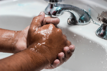 Man washing hands under faucet in sink.