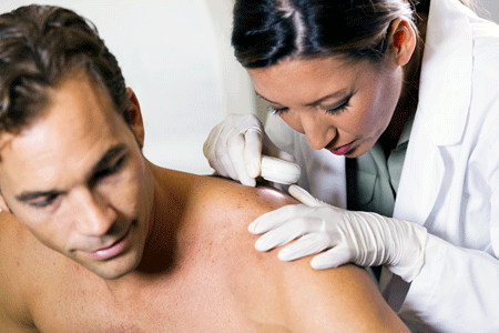 Female dermatologist examining male patient with dermascope, looking for signs of skin cancer.