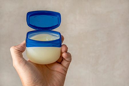 The hand of a male person holds a container with petroleum jelly 