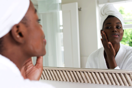 Young woman looking at her face in bathroom mirror.